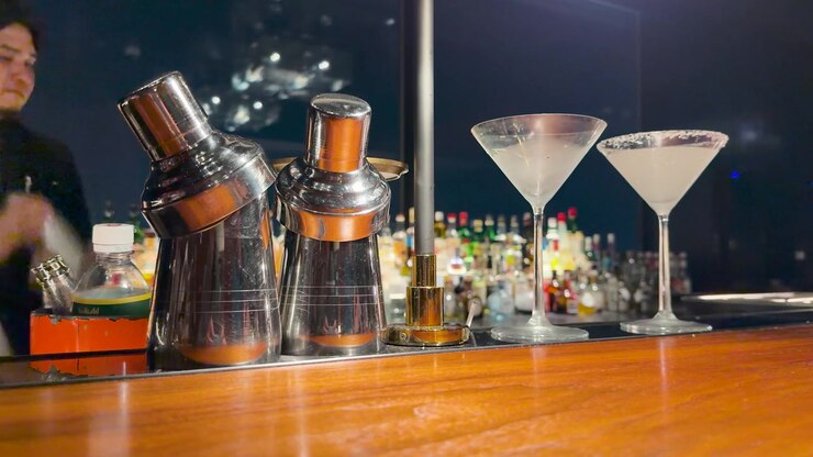 Un barista professionista agita uno shaker per cocktail dietro un bancone di legno con bicchieri da martini