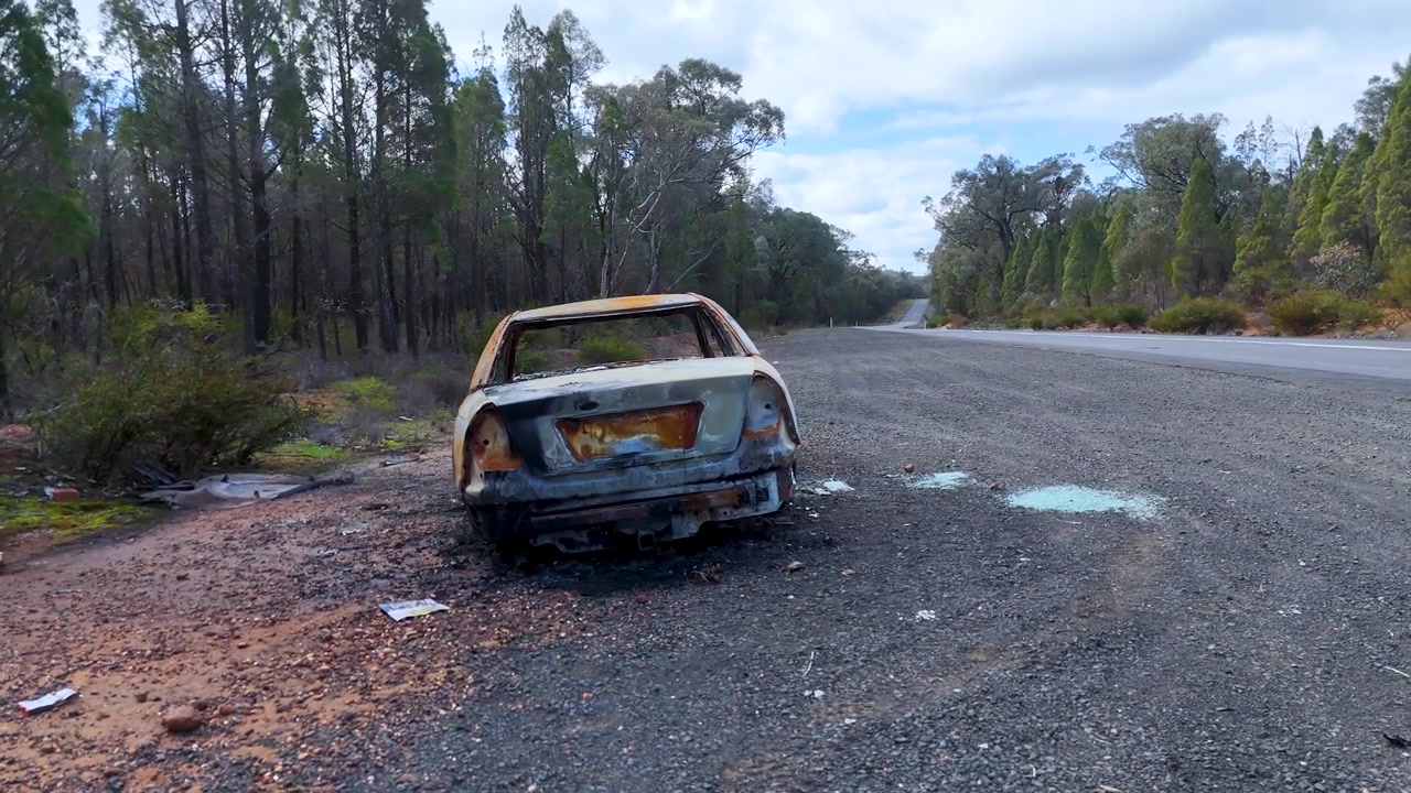 A charred, abandoned sedan sits on a remote highway shoulder in Coonabarabran, New South Wales.