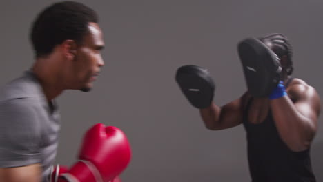 Toma-De-Estudio-En-Tiempo-Real-De-Un-Boxeador-Masculino-Entrenando-Con-Un-Entrenador-Que-Usa-Guantes-De-Boxeo-O-Manoplas-Y-Practica-Para-La-Pelea-1