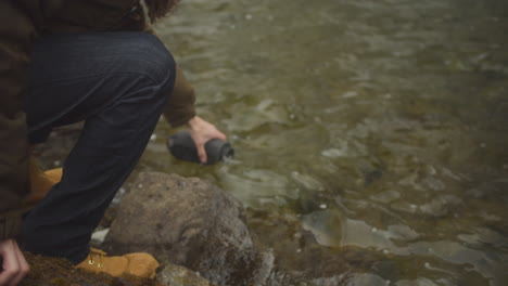 wanderer schöpft und füllt seinen isolierten becher mit süßwasser aus dem fluss