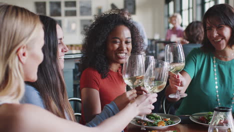 group of female friends making a toast at meal in restaurant