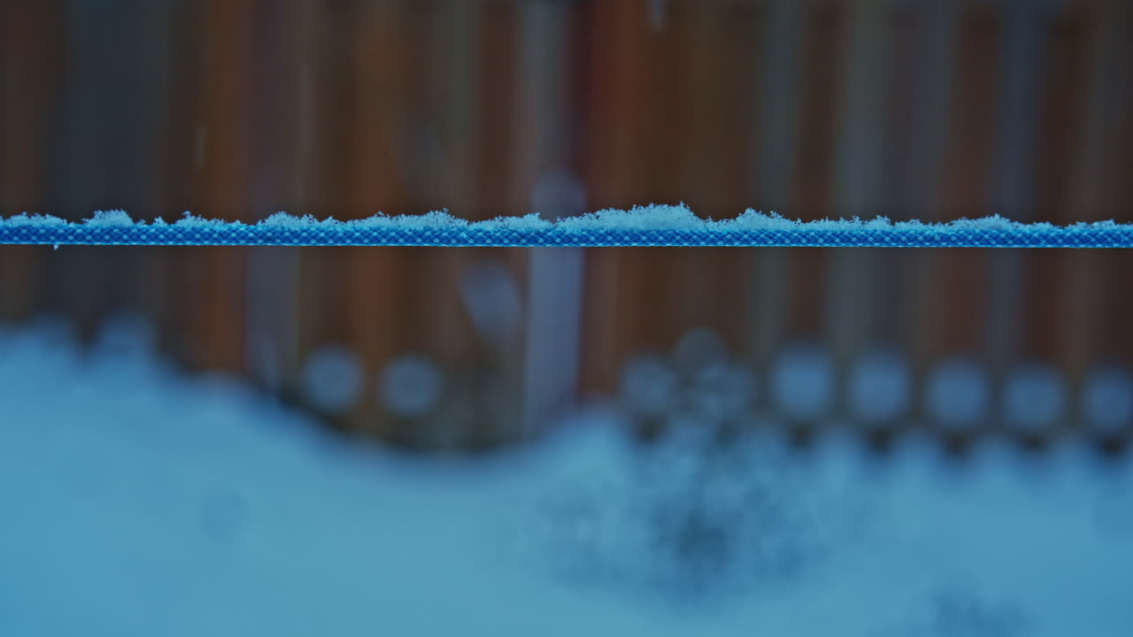 First snow gently accumulating on a backyard clothesline as light snowfall begins. Lateral movement