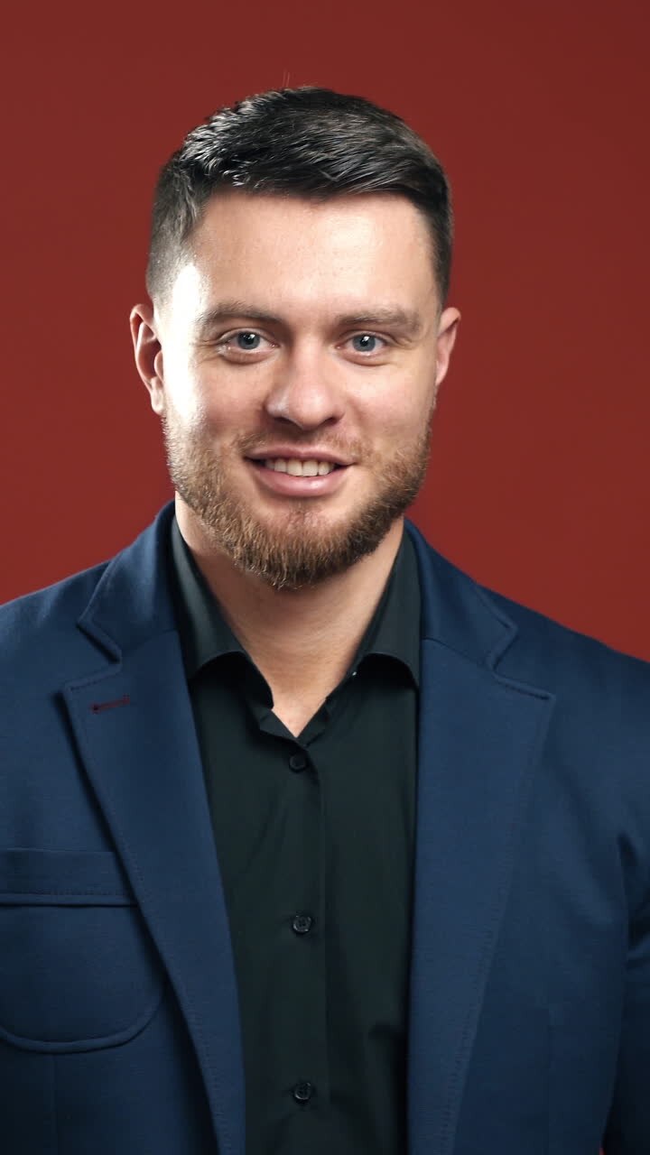 Confident businessman. Half-length portrait of brunette man isolated on claret studio. Young businessman in dark suit smiling on camera. Vertical video