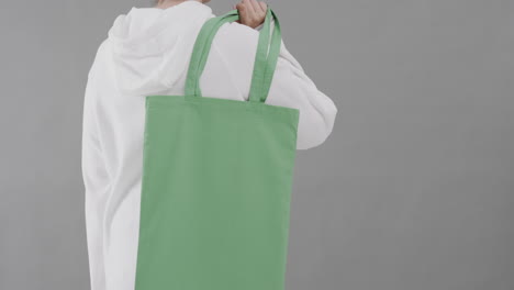 mujer caucásica con capucha blanca sosteniendo una bolsa verde sobre un fondo gris, espacio de copia, cámara lenta