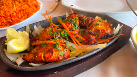 traditional indian tandoori chicken tikka with onions on a very hot plate with steam smoke in a restaurant, 4k shot