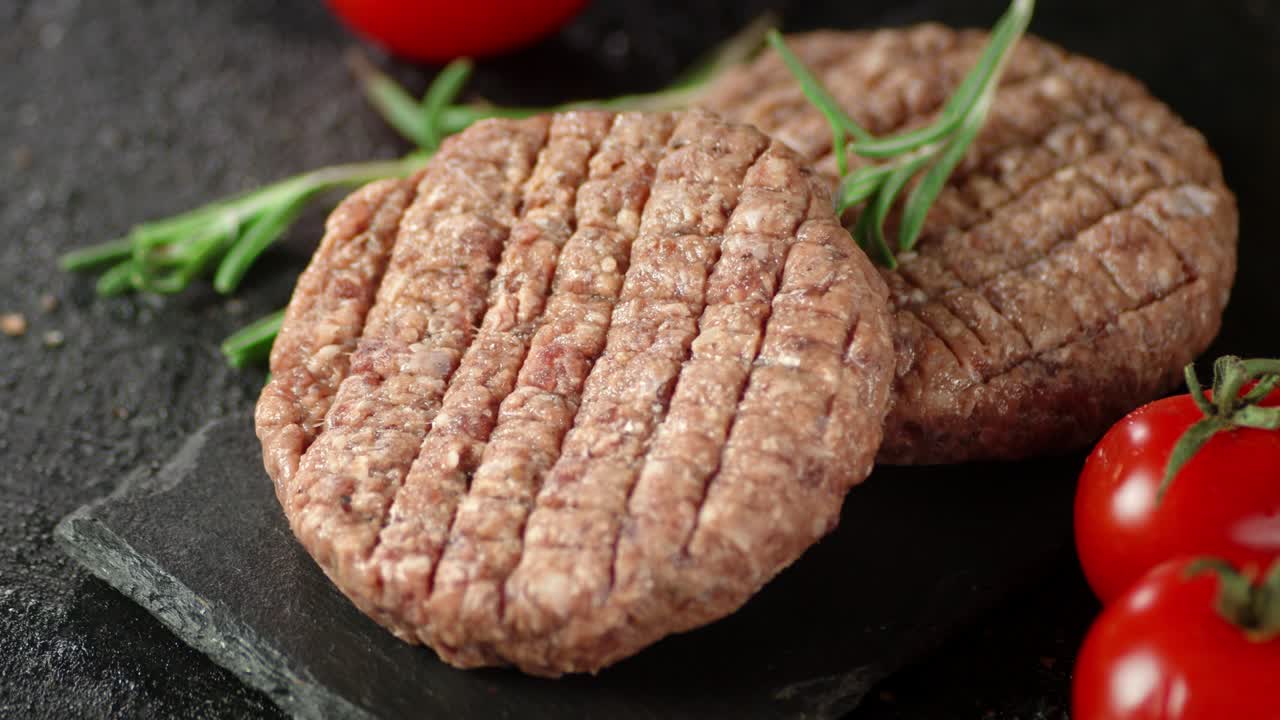 hamburguesa cruda en una tabla con romero y tomates gira.