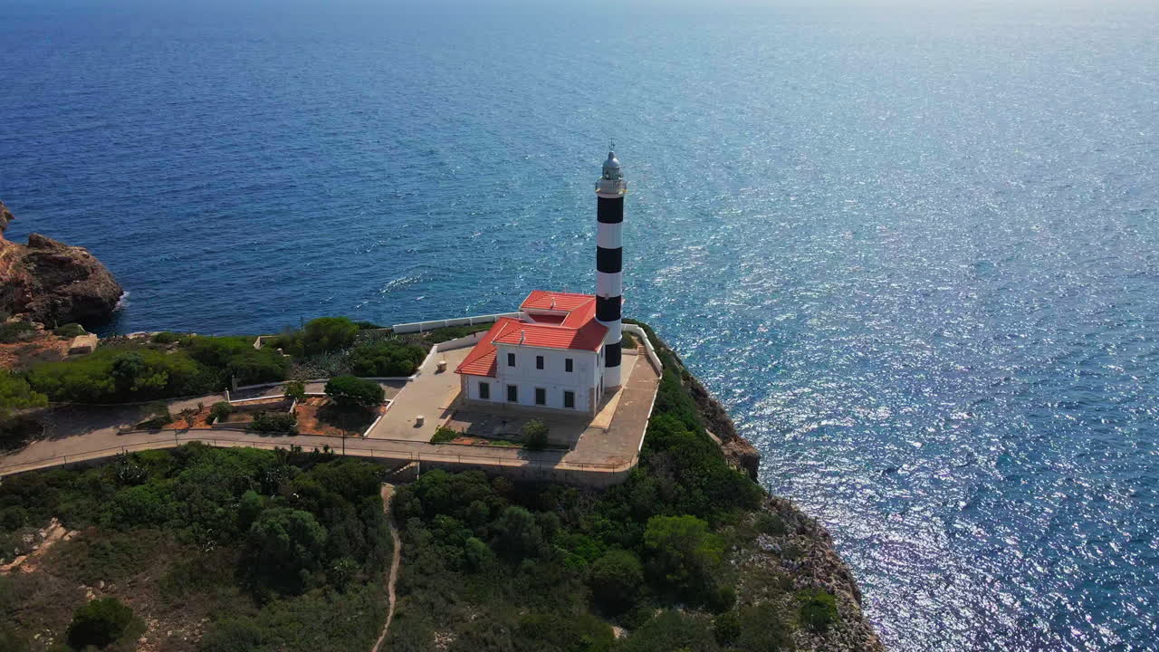 Orbita aerea di un faro spagnolo con l'oceano scintillante e la rivelazione di un villaggio durante l'estate in una calda giornata tropicale.