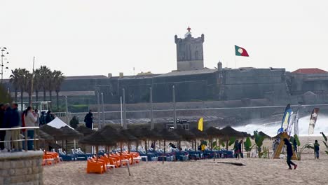 Das-Fotografenteam-Und-Die-Surfer-Warten-Auf-Das-Große-Ereignis-Mit-Perfekten-Wellen-Und-Den-Besten-Tube-Fahrern-In-Carcavelos-In-Einem-Perfekten-Kapitel-Mit-Fort-Saint-Julian-Und-Der-Portugiesischen-Flagge-Im-Hintergrund