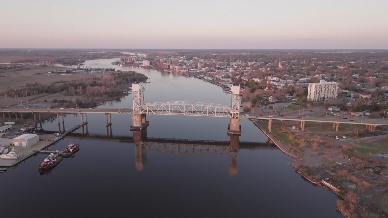 A 4k drone shot tracking any from a coastal town with a bridge and the reflection in the calm water at sunset