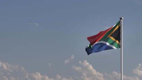 flag of south africa on right of frame, flutters against sunny sky