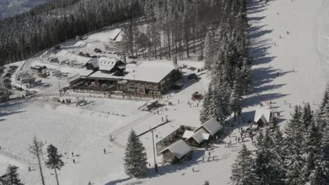 Estación-De-Esquí-De-Kope-En-Las-Montañas-De-Pohorje-Con-Visitantes-En-La-Pista-Nevada-Y-Trineos,-Tiro-Aéreo-A-La-Derecha