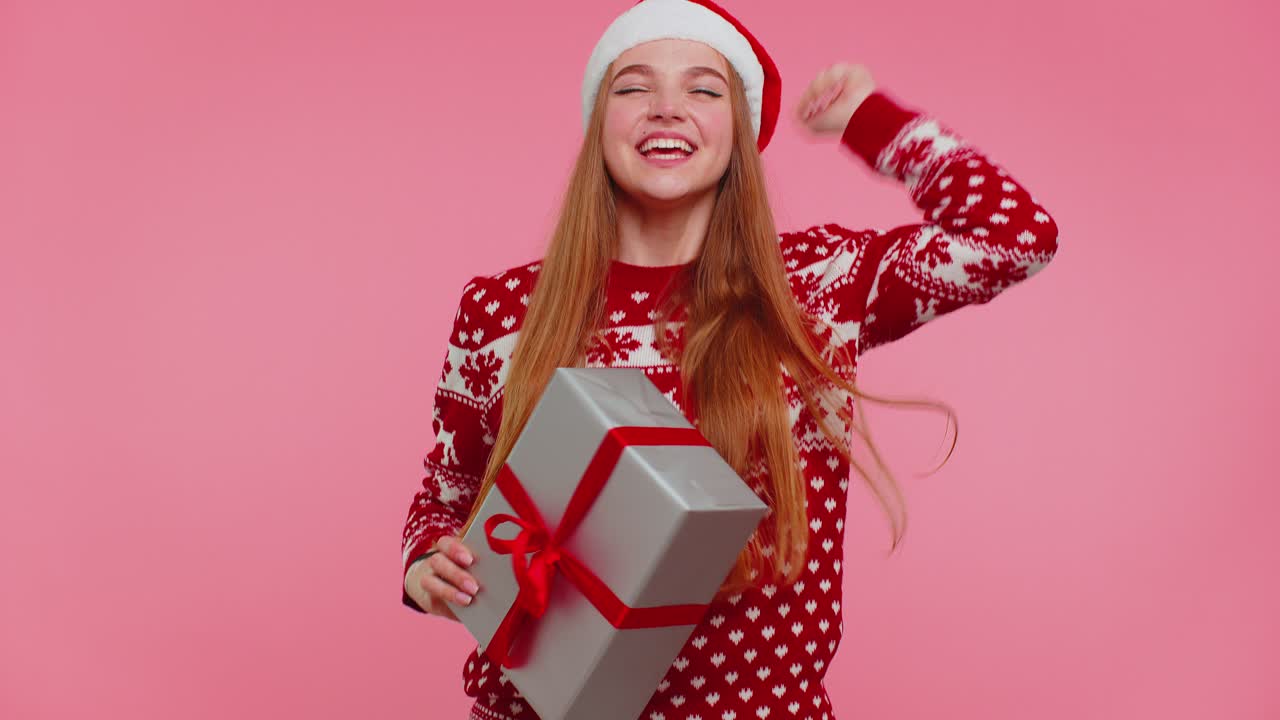 Cheerful girl in christmas santa sweater getting present gift box expressing amazement happiness