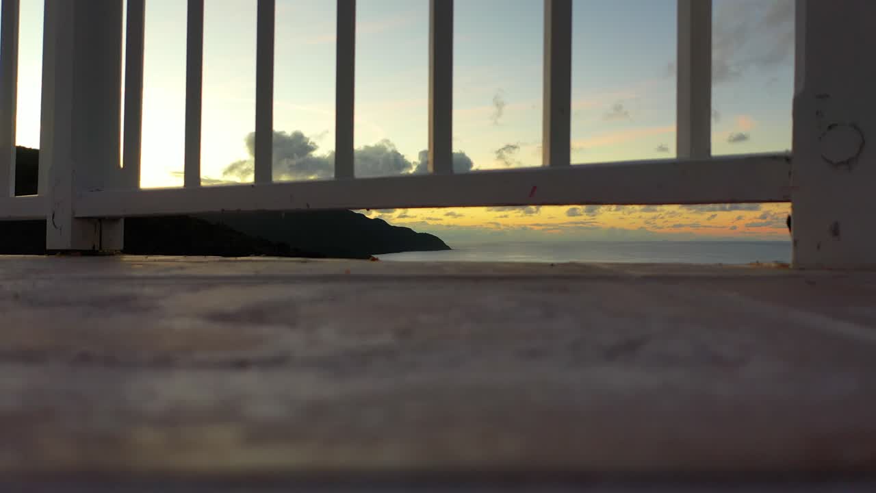 Cinematic close-up of a white fence, ocean waves and dense forest visible through its slats, blending coastal charm with wild, untouched natural scenery