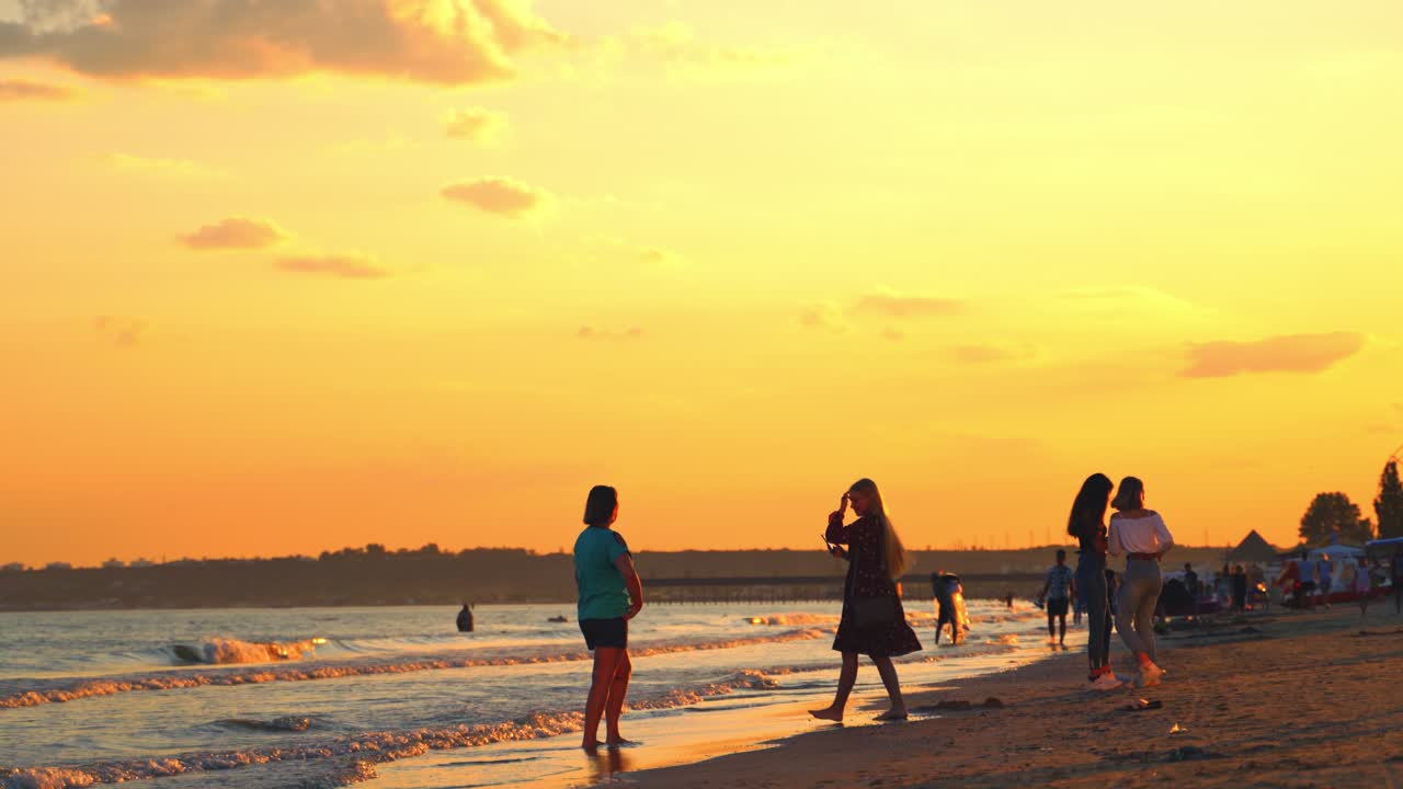 Young women doing photography on the seashore. Beautiful sunset over the sea water and people taking photos in the evening.