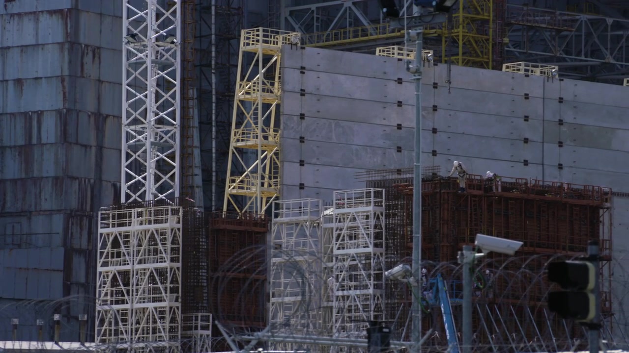Camera tilts down the old Chernobyl sarcophagus structure and construction site.