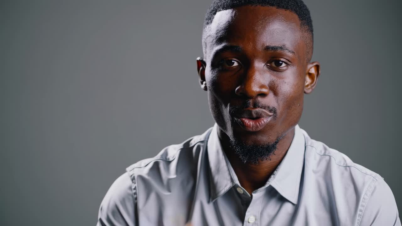 Close-up video shot of a man speaking, with a neutral gray background