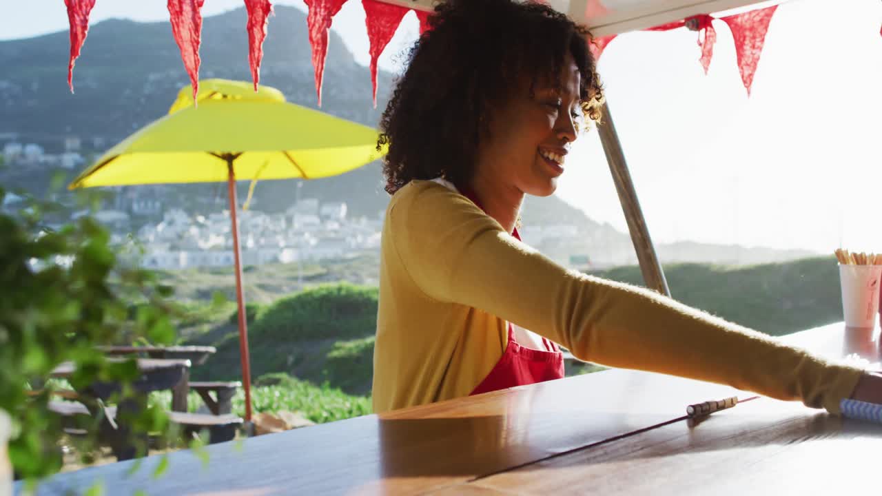 아프리카계 미국인 여성 이 음식 트럭 을 청소 하는 동안 미소 짓고 아프론 을 입고 있다