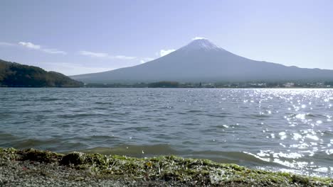 vista de ángulo bajo del monte fuji en la distancia con el lago y pequeñas olas rompiendo en la playa timelapse