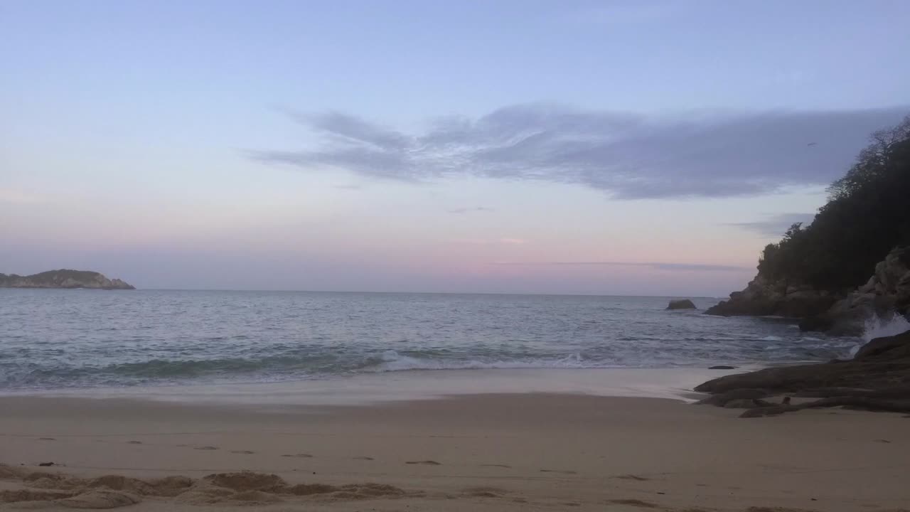 Time-lapse as the sunsets over the ocean. Sand and rocks can be seen on the sides.