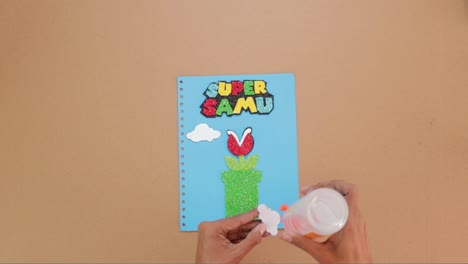 hands gluing paper art on handmade notebook cover, video game themed notebook