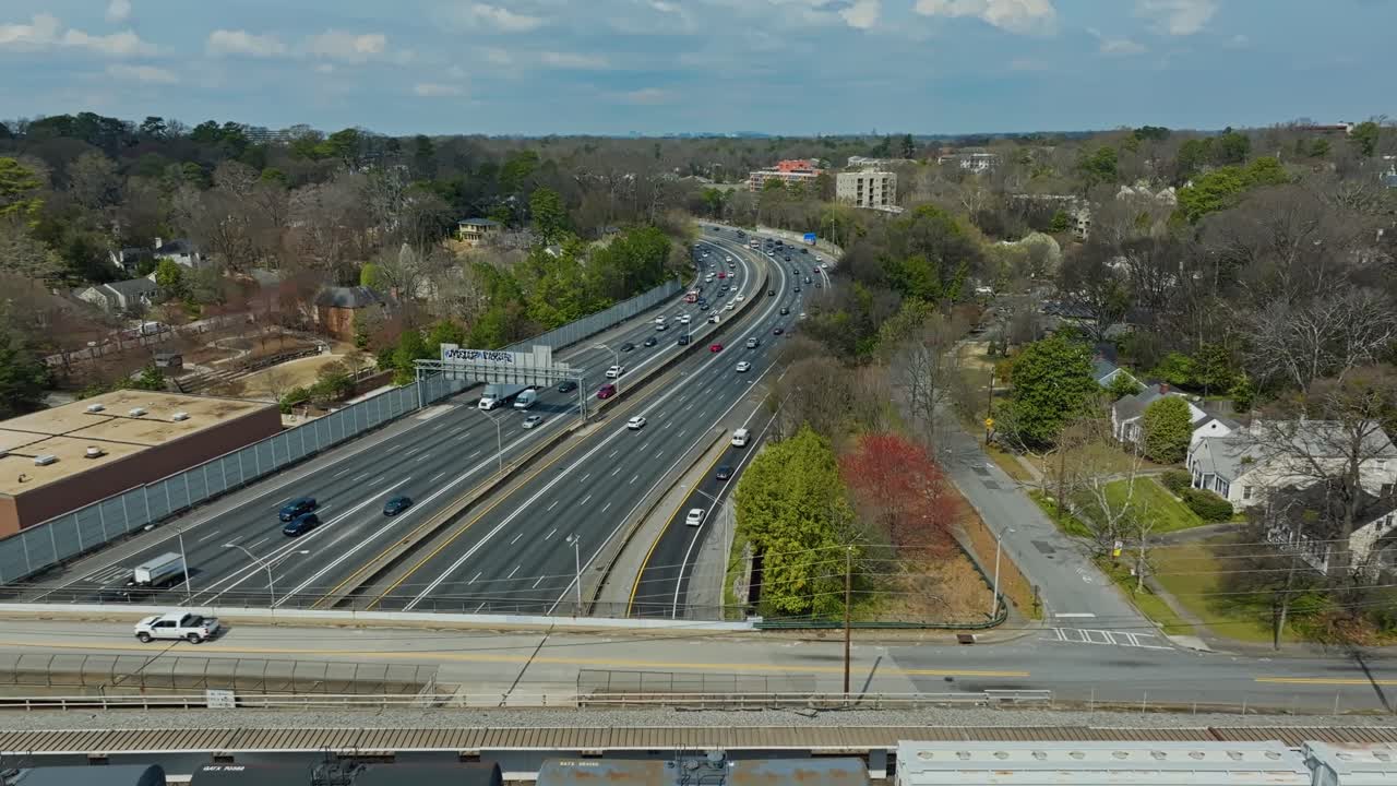 Aerial flyover parking freight cargo train on bridge over american highway with driving cars. Sunny day in suburb of american town in spring season. Wide shot.