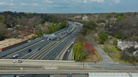 aerial flyover parking freight cargo train on bridge over american highway with driving cars. sunny day in suburb of american town in spring season. wide shot.