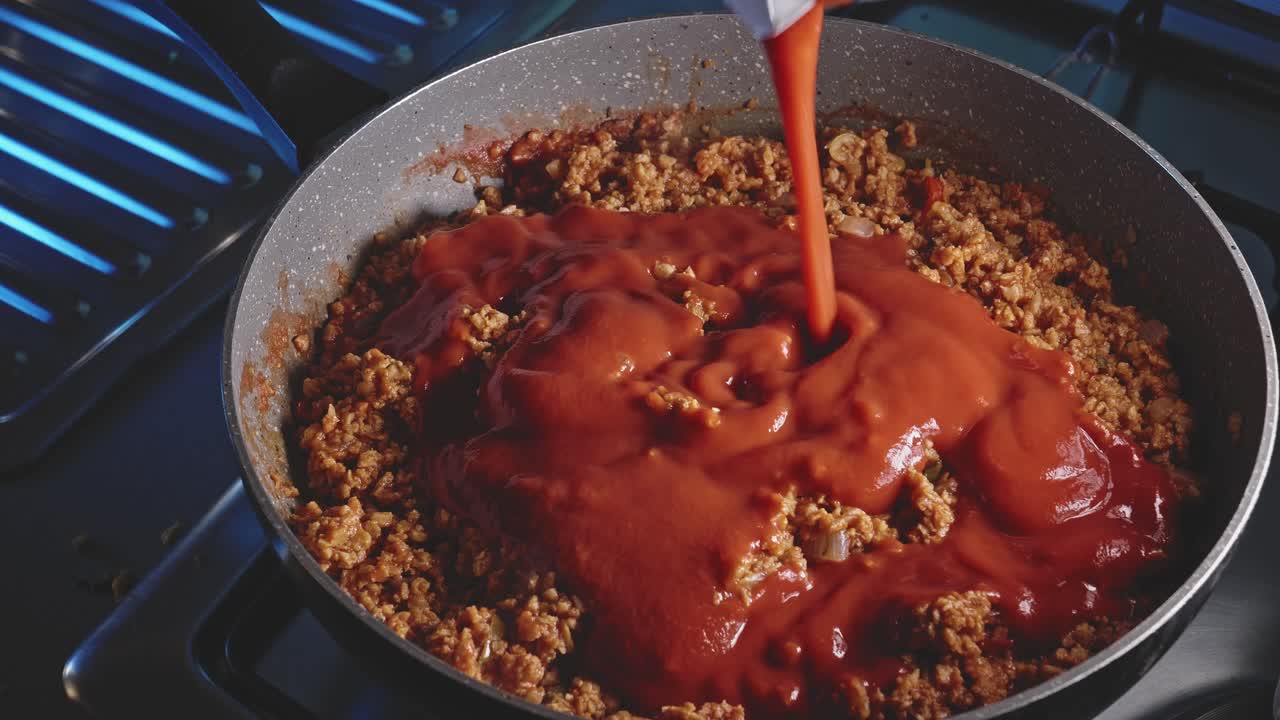 Pouring tomato sauce in a pot full of vegetarian bolognese, then mixing it all with a wooden spoon, close up view