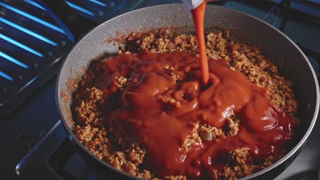 pouring tomato sauce in a pot full of vegetarian bolognese, then mixing it all with a wooden spoon, close up view