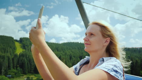 an active woman in the cabin of a ski lift photographs beautiful views of mountains and forests holi