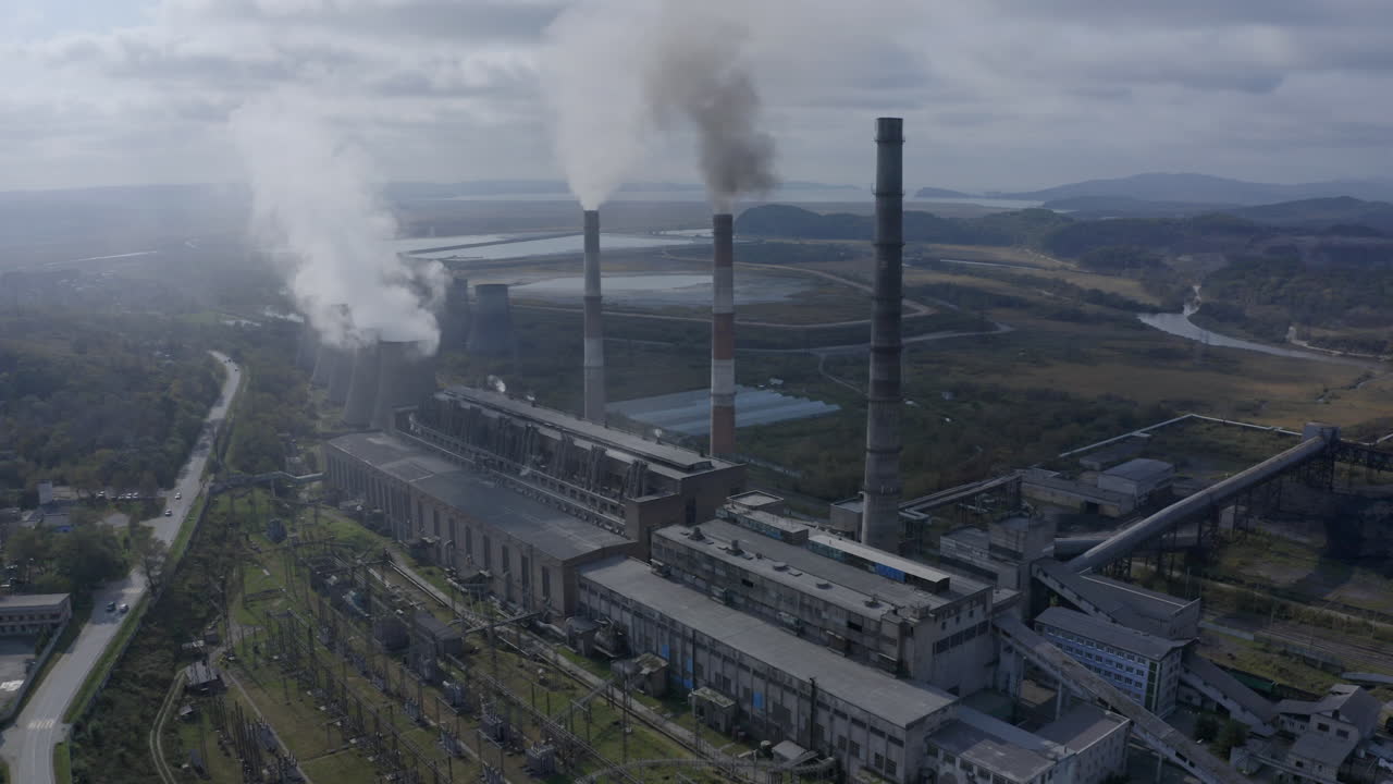 Una centrale elettrica a carbone con ciminiere che rilasciano fumo denso e pesante nell'aria, in una giornata luminosa, soleggiata e nuvolosa