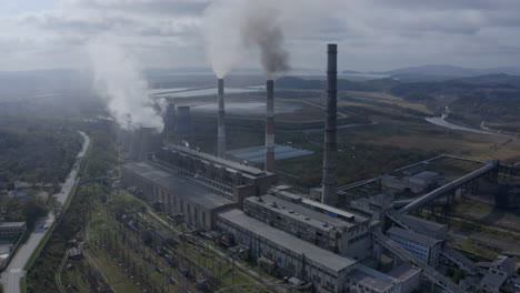 a coal-fired power plant with chimneys and funnels releasing dense heavy smoke into the air, on a bright, sunny, cloudy day