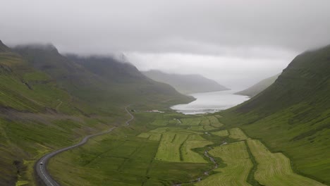 Inclinación-Aérea-Hacia-Abajo-Del-Fiordo-Occidental-De-Sugandafjordur-Durante-El-Día-Nublado-En-Islandia---Montañas-Verdes-Y-Camino-Durante-El-Día-Brumoso---Toma-Amplia