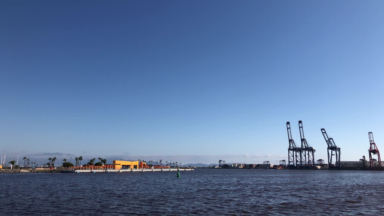 clip de cámara lenta de un puerto industrial con contenedores industriales y grúas en el fondo y un hermoso cielo azul con algunas gaviotas y el mar con olas