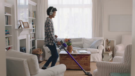 happy young man dancing at home using vacuum cleaner celebrating success listening to music wearing headphones having fun dance in living room on weekend
