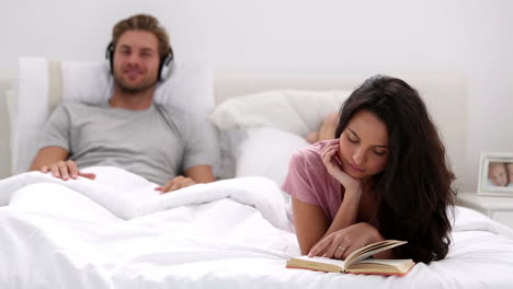 mujer leyendo un libro mientras su pareja escucha música