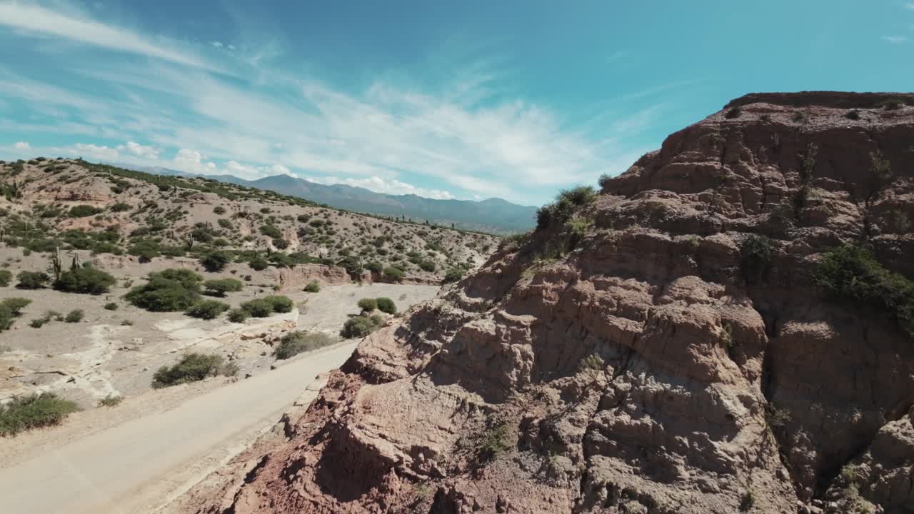 Drone FPV a bassa quota sopra una strada nel deserto che passa vicino alle montagne.