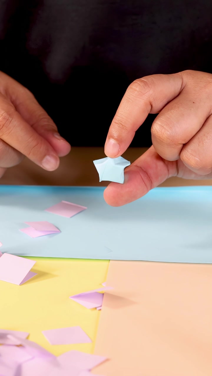 Mani di una persona creano una stella origami blu usando carta pastello, primo piano, illuminazione soffusa.