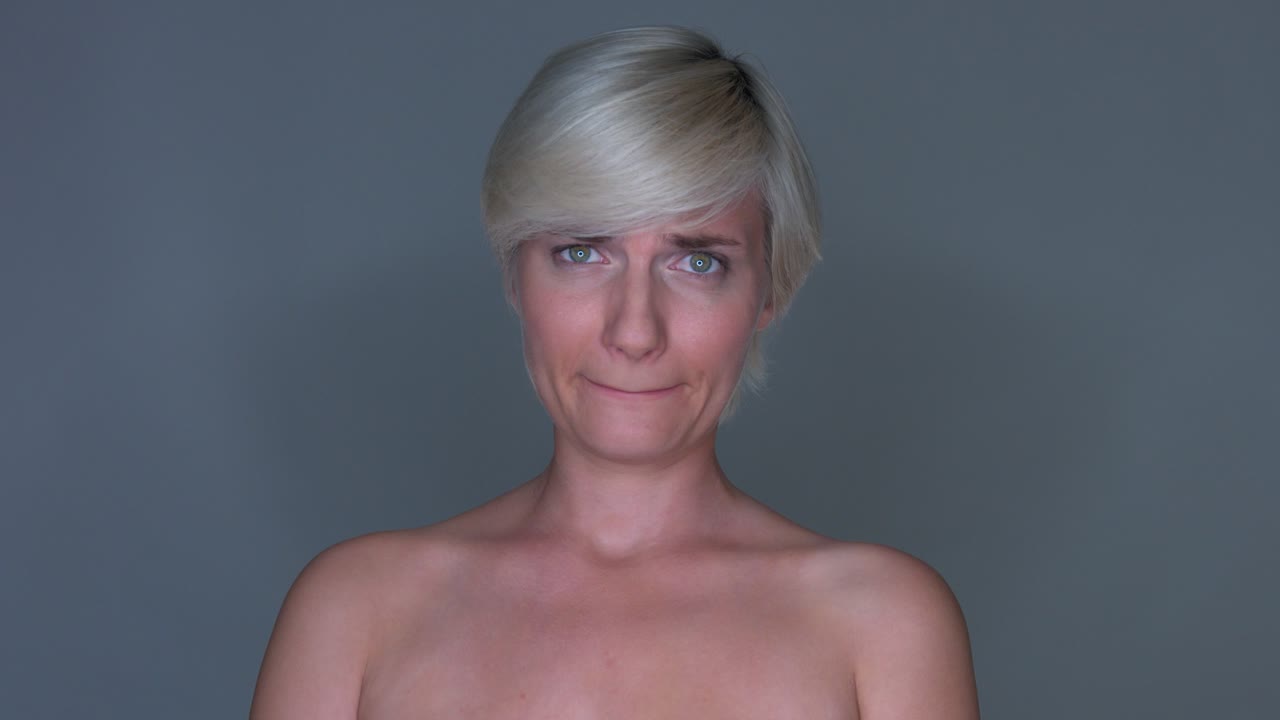 Slow zoom in of a female model giving a worried expression and being tilt-lipped, on a sealess grey studio background