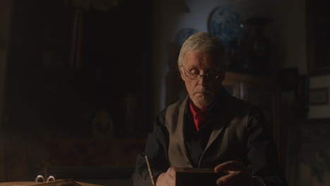 older passionate man evaluates an old watch in his office at night