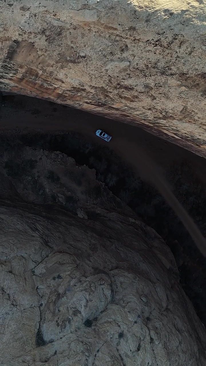 SUV Bianco in Movimento su Strada in Canyon Profondo Sotto Scogliere di Arenaria, Ripresa Drone Verticale Dall'Alto