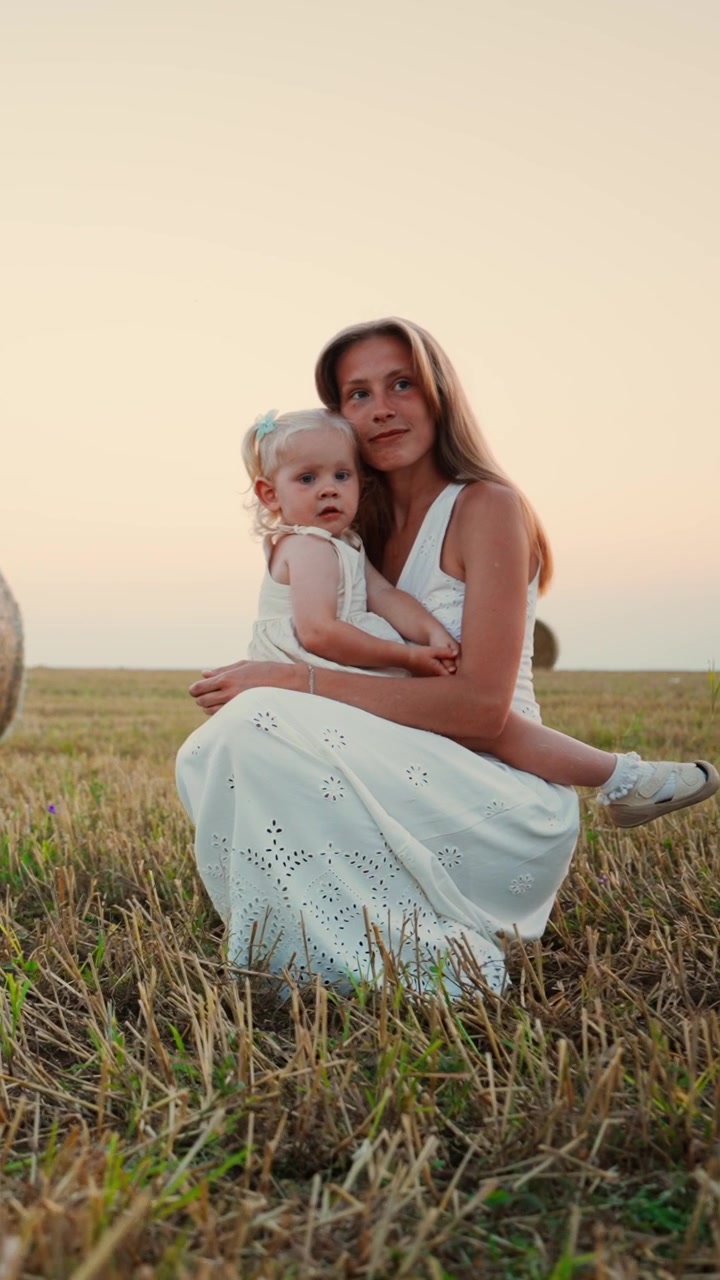 Mutter und ihre kleine Tochter sitzen auf abgeerntetem Feld bei Sonnenuntergang