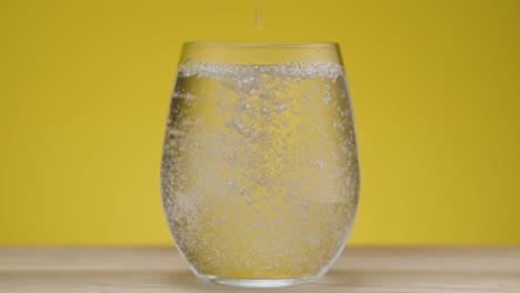 pouring sparkling water in a clear transparent glass with yellow background