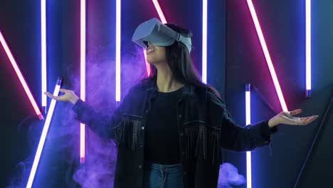 young woman looks around and wonders how amazing  in the vr headset. virtual reality helmet on color lighting smoke background