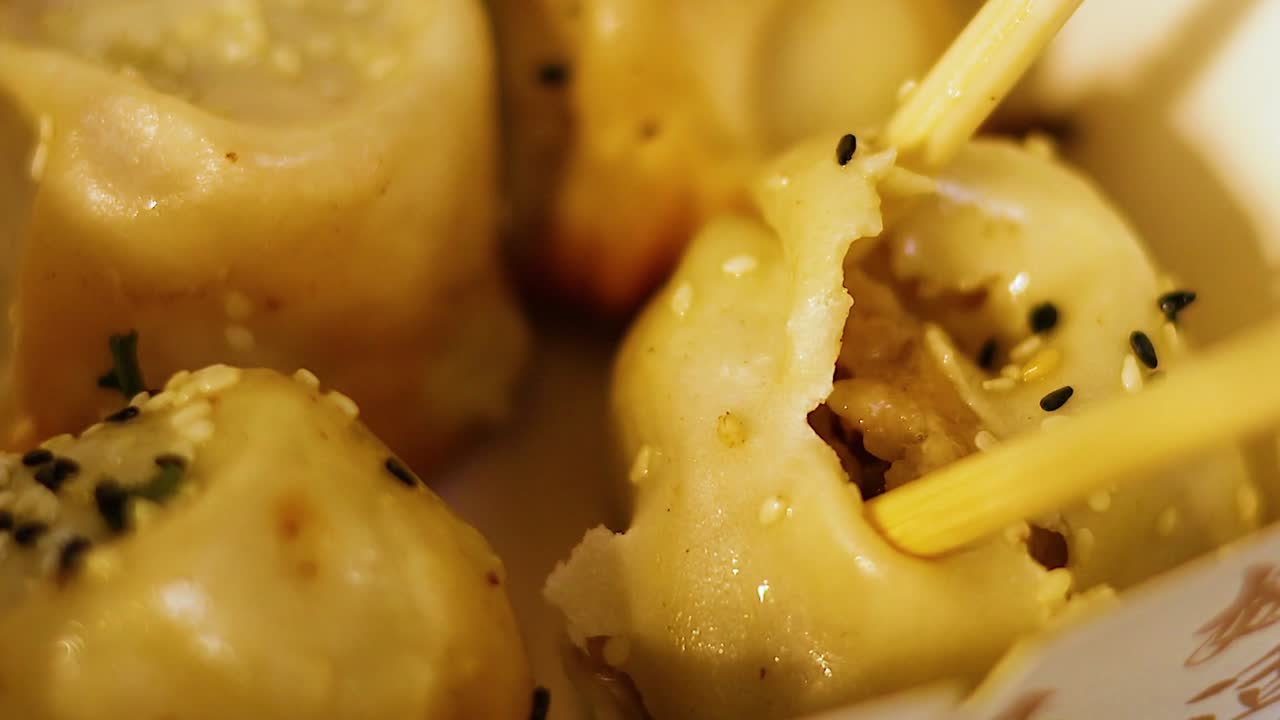 Macro view of wooden chopsticks piercing a sesame-topped dumpling to reveal the savory filling