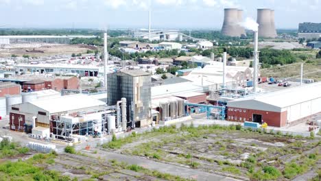 Industrial-warehouse-power-plant-refinery-buildings-under-smokestack-wasteland-aerial-view-push-in