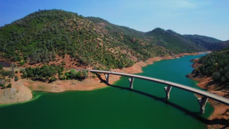 Aerial-panning-drone-shot-of-cars-crossing-a-bridge-over-a-lake-at-Don-Pedro-Reservoir-in-California