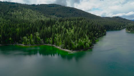 Drone-footage-of-a-mountain-lake-in-Canada-with-blue-and-green-water,-coniferous-forests,-and-forest-houses-on-the-shore