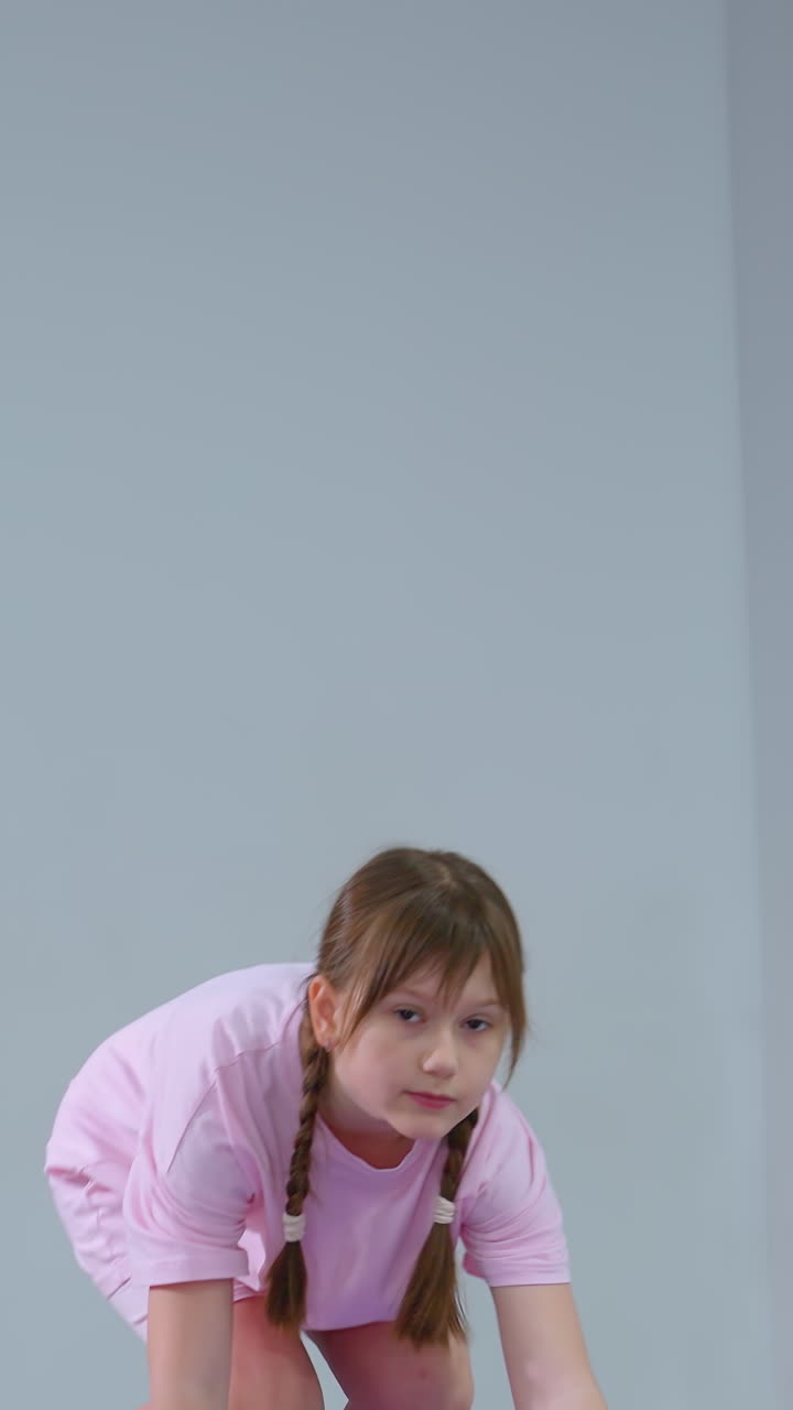 niño pequeño equilibrando en almohadillas de caucho amarillas, extendiendo la mano hacia adelante para la estabilidad, el fondo presenta equipos de gimnasia, incluidos rodillos de espuma y un armario de almacenamiento