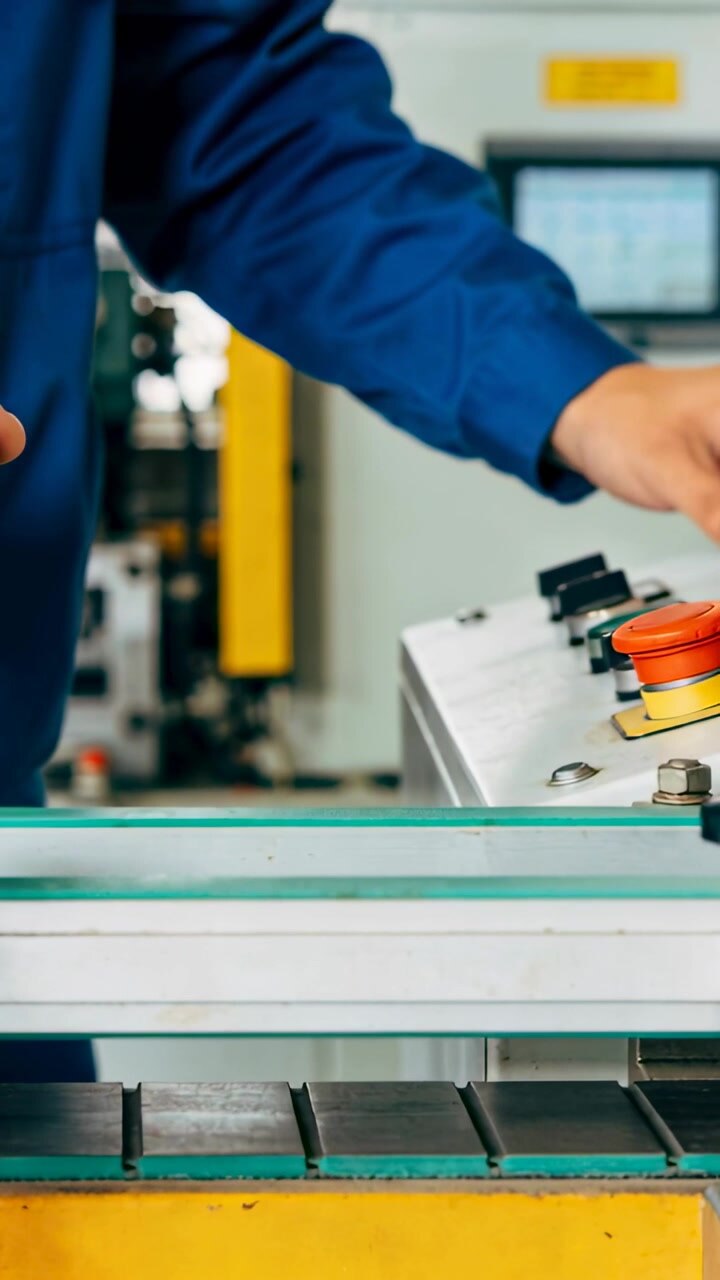 Vertical video: Holding clamp at machine, tech in blue coat pressing estop and adjusting controls