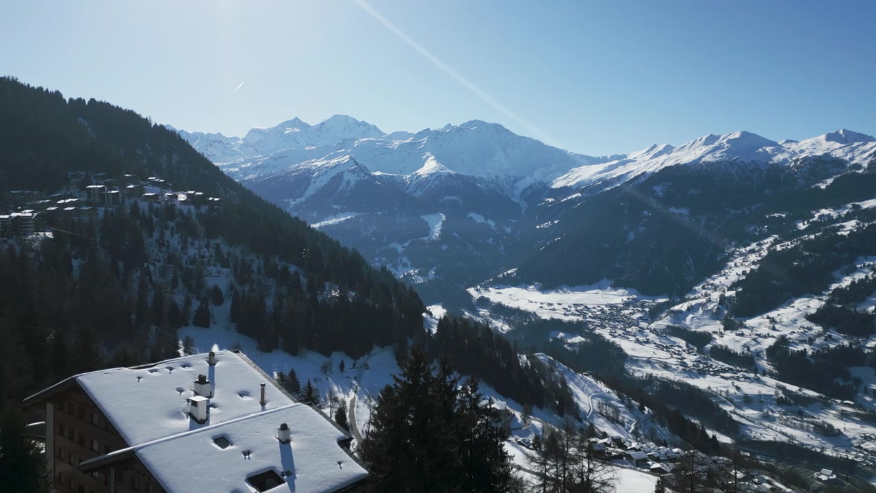 Vista aérea de edificios, árboles y montañas cubiertos de nieve a lo lejos en Verbier, Suiza.